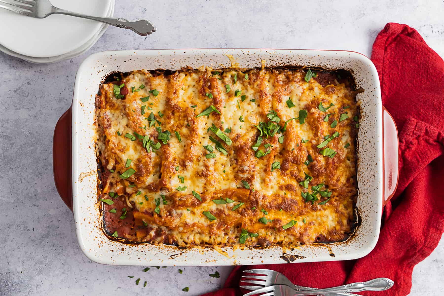 Top view of cooked cheese manicotti in a rectangular oven dish and white plates on the side. 