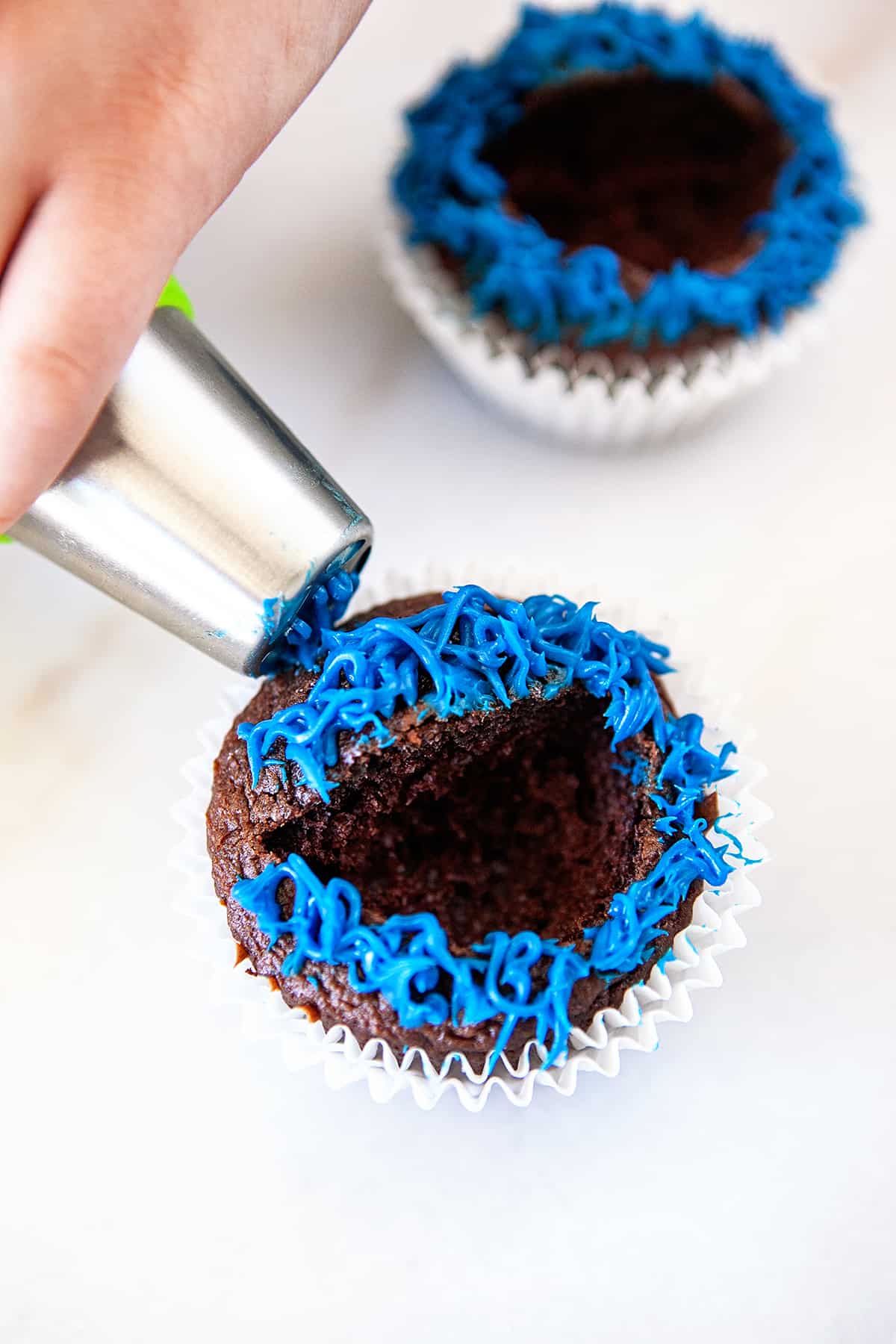 Piping blue icing on a cupcake