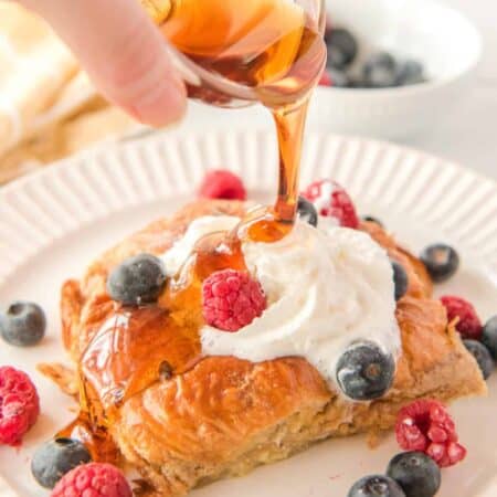 Pouring maple syrup on a slice of croissant French toast bake.