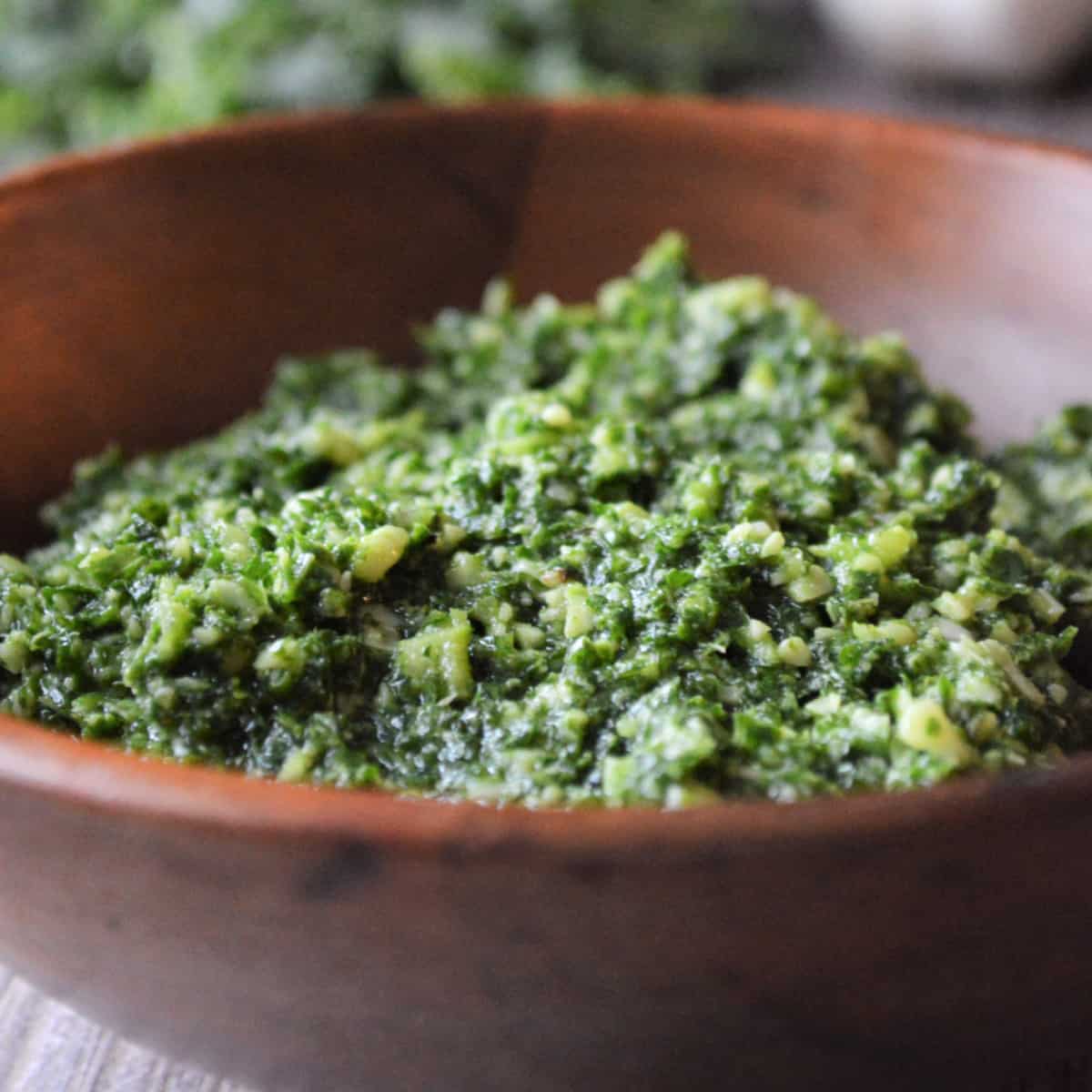 Square photo of a wooden bowl with kale pesto recipe. 