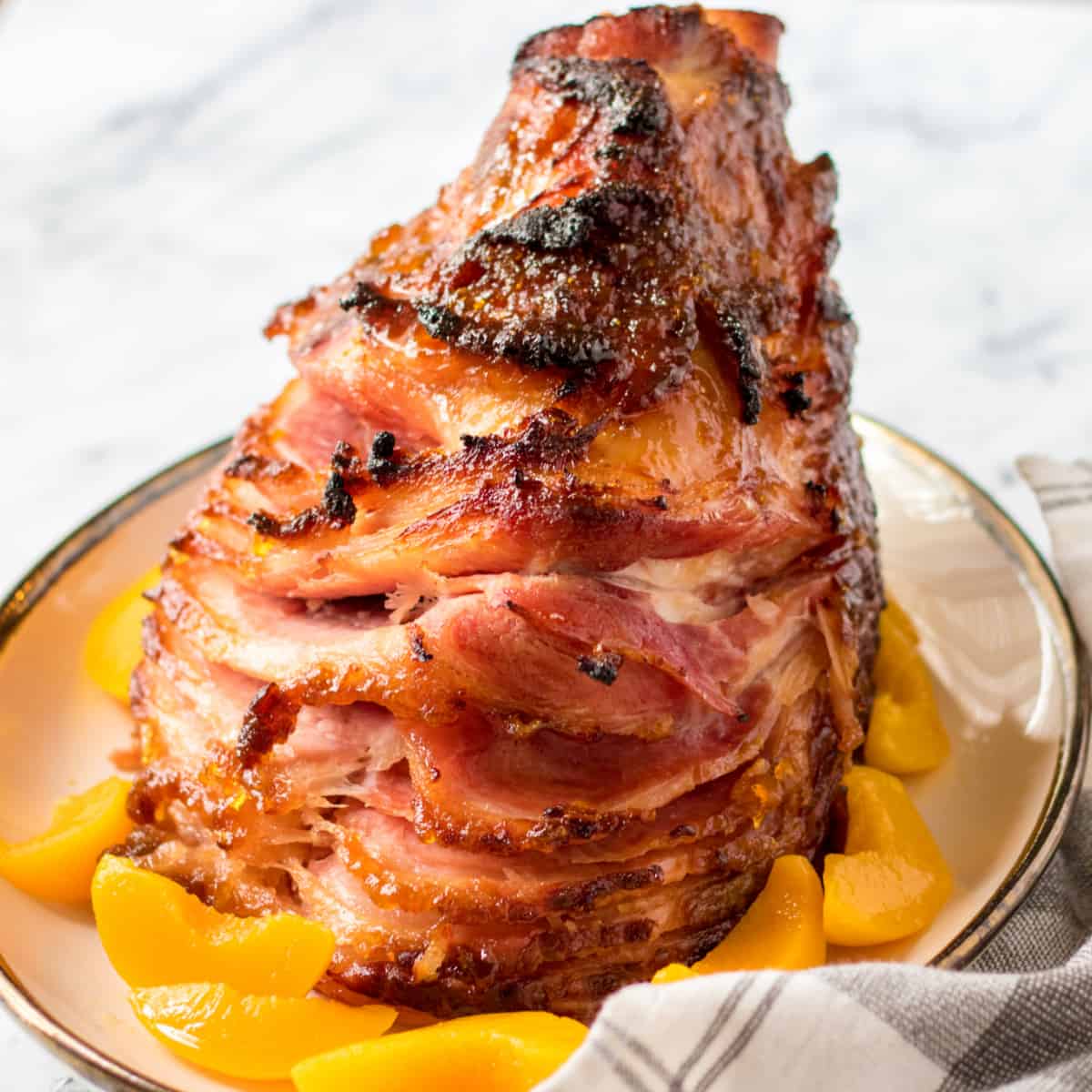 Peach Glazed Spiral Ham on a platter surrounded by peaches