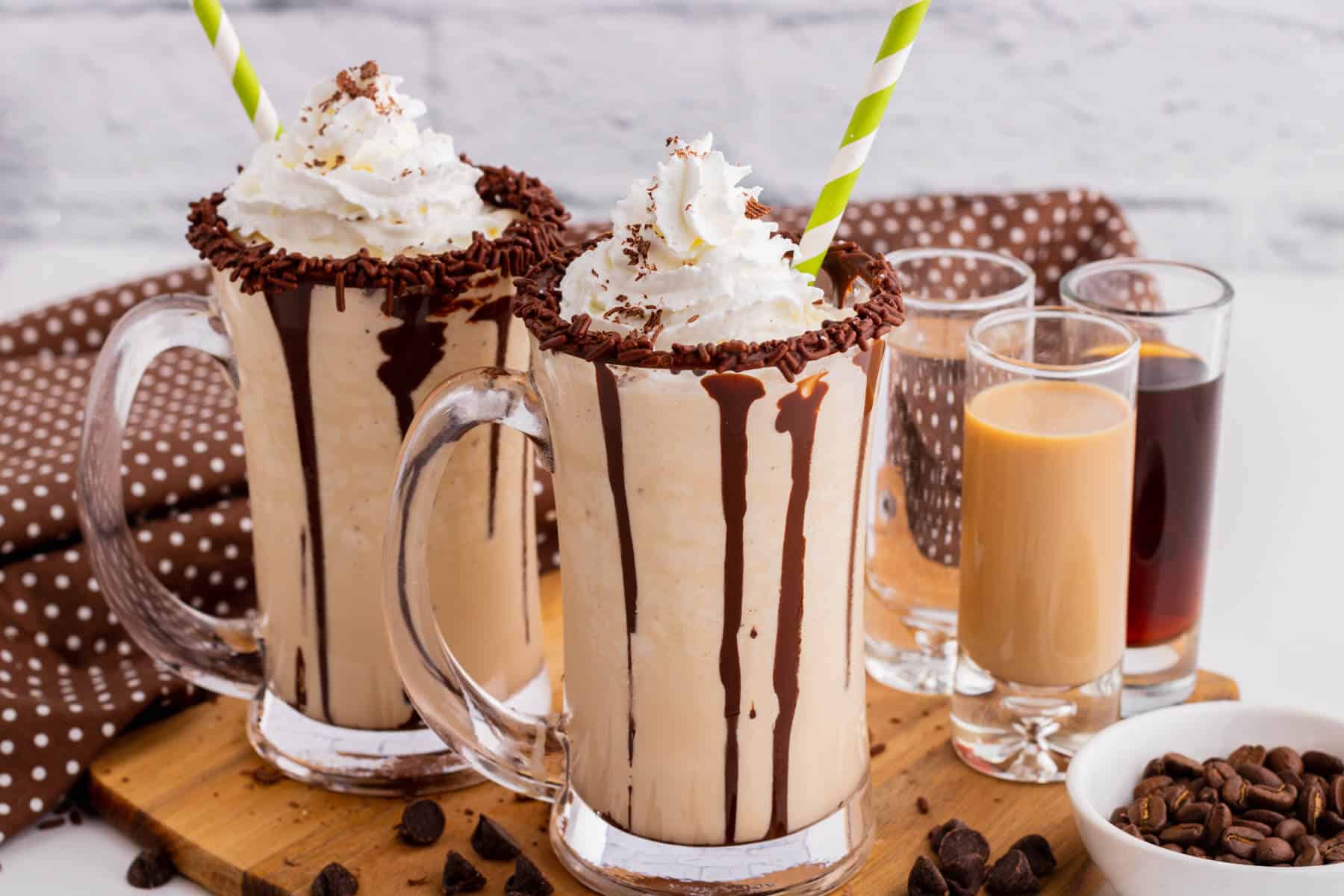 Two chocolate rimmed glass mugs containing frozen mudslide, whipped cream, and chocolate sauce.