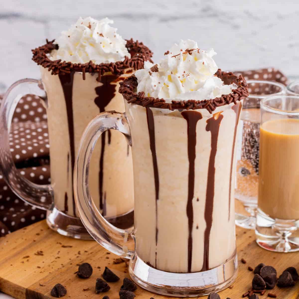 Two chocolate rimmed glass mugs containing frozen mudslide, whipped cream, and chocolate sauce.