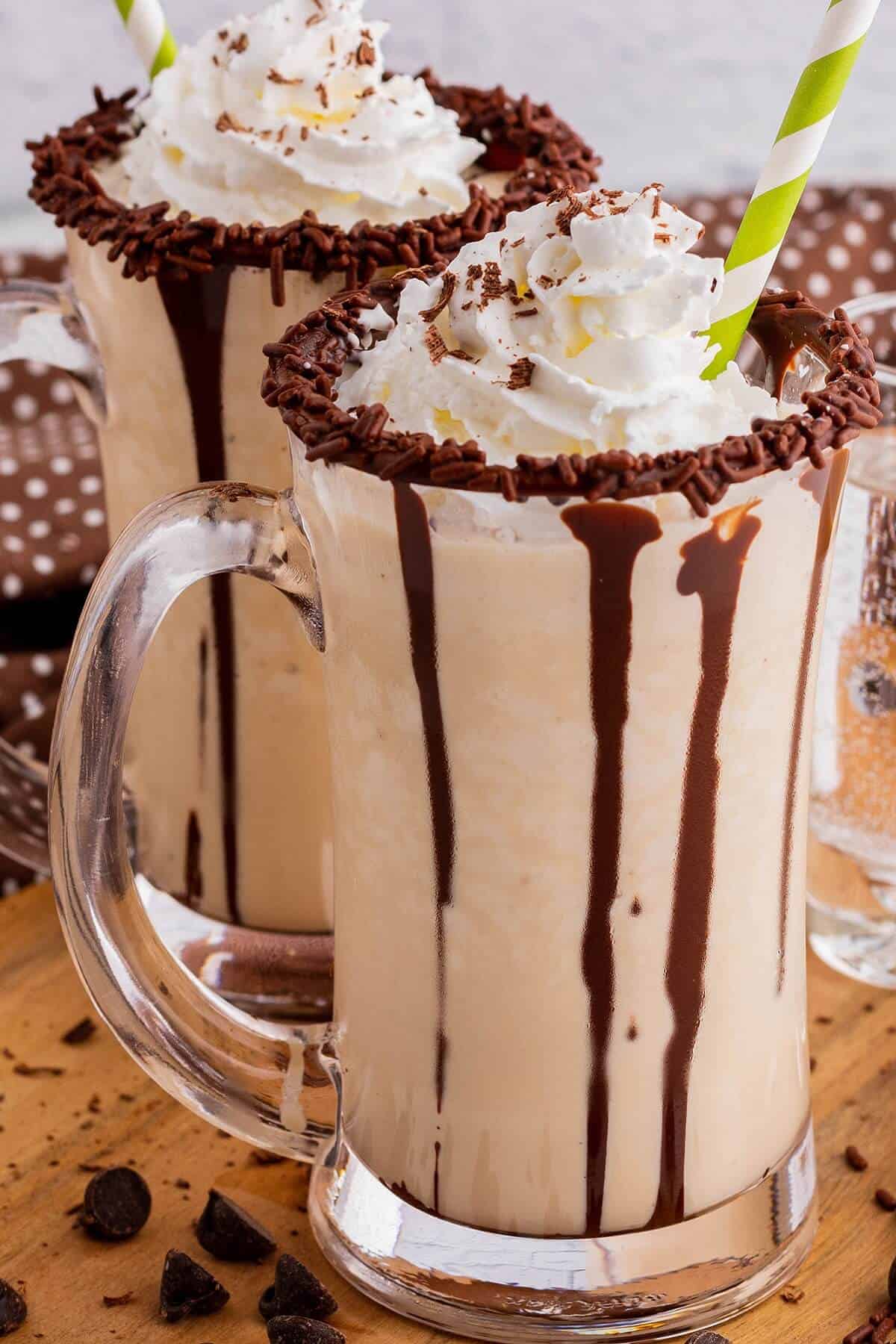 Two chocolate rimmed glass mugs containing frozen mudslide, whipped cream, and chocolate sauce.