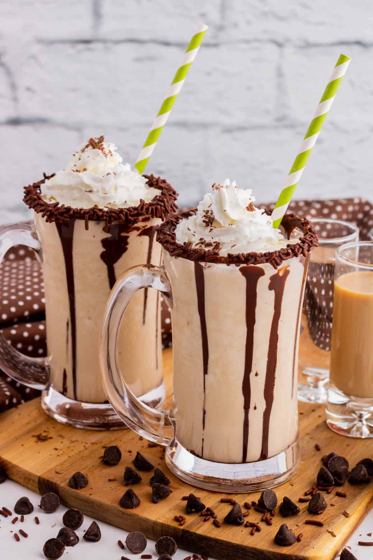 Two chocolate rimmed glass mugs containing frozen mudslide, whipped cream, and chocolate sauce.