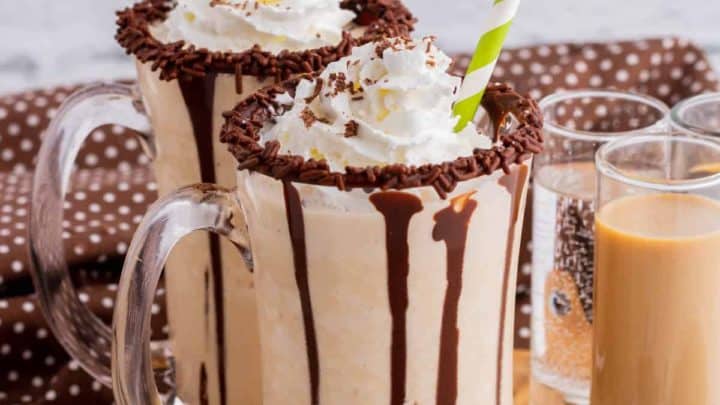 Two chocolate rimmed glass mugs containing frozen mudslide, whipped cream, and chocolate sauce.