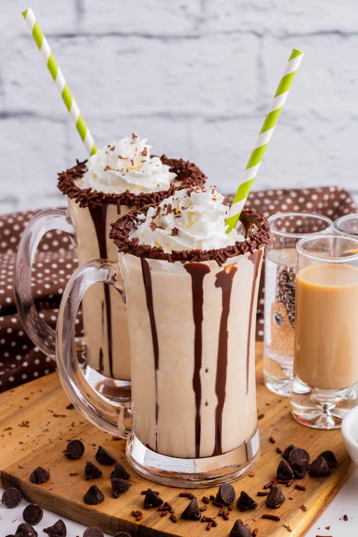 Two chocolate rimmed glass mugs containing frozen mudslide, whipped cream, and chocolate sauce.