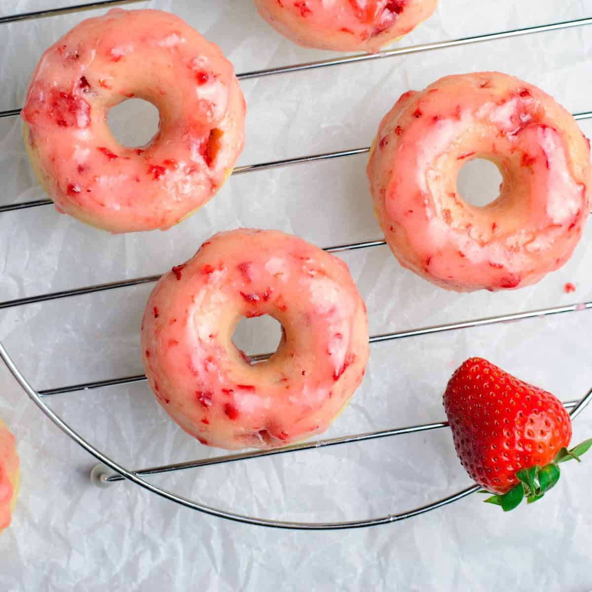 Overhead square of doughnuts on a cooling rack with a strawberry. 