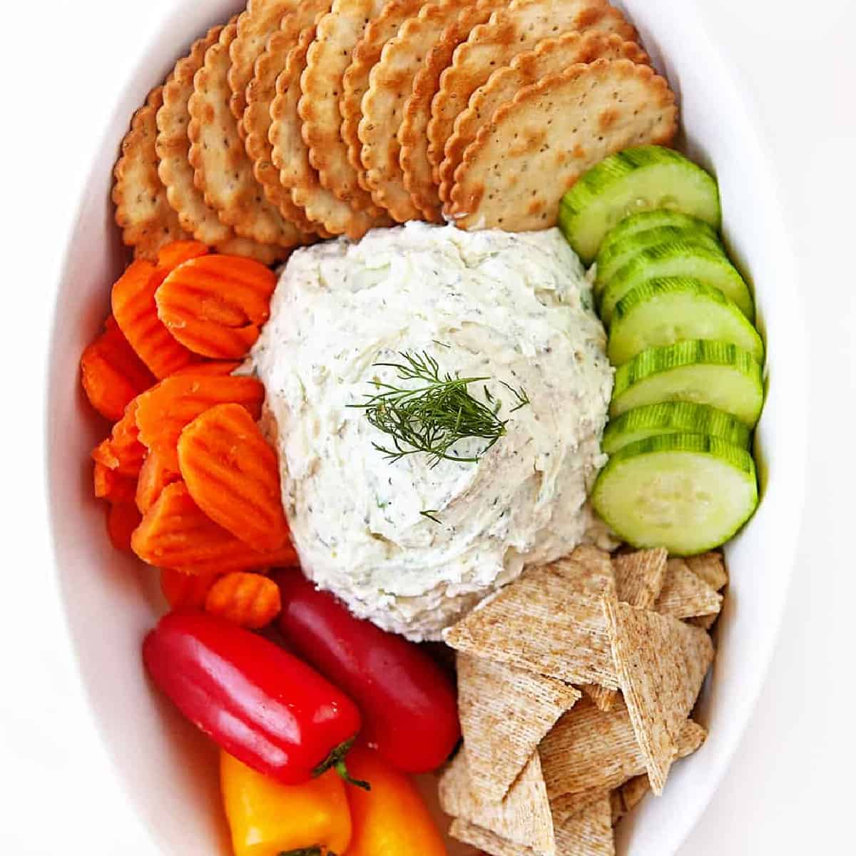 Overhead square photo of homemade boursin with veggies and crackers in a small white casserole dish. 