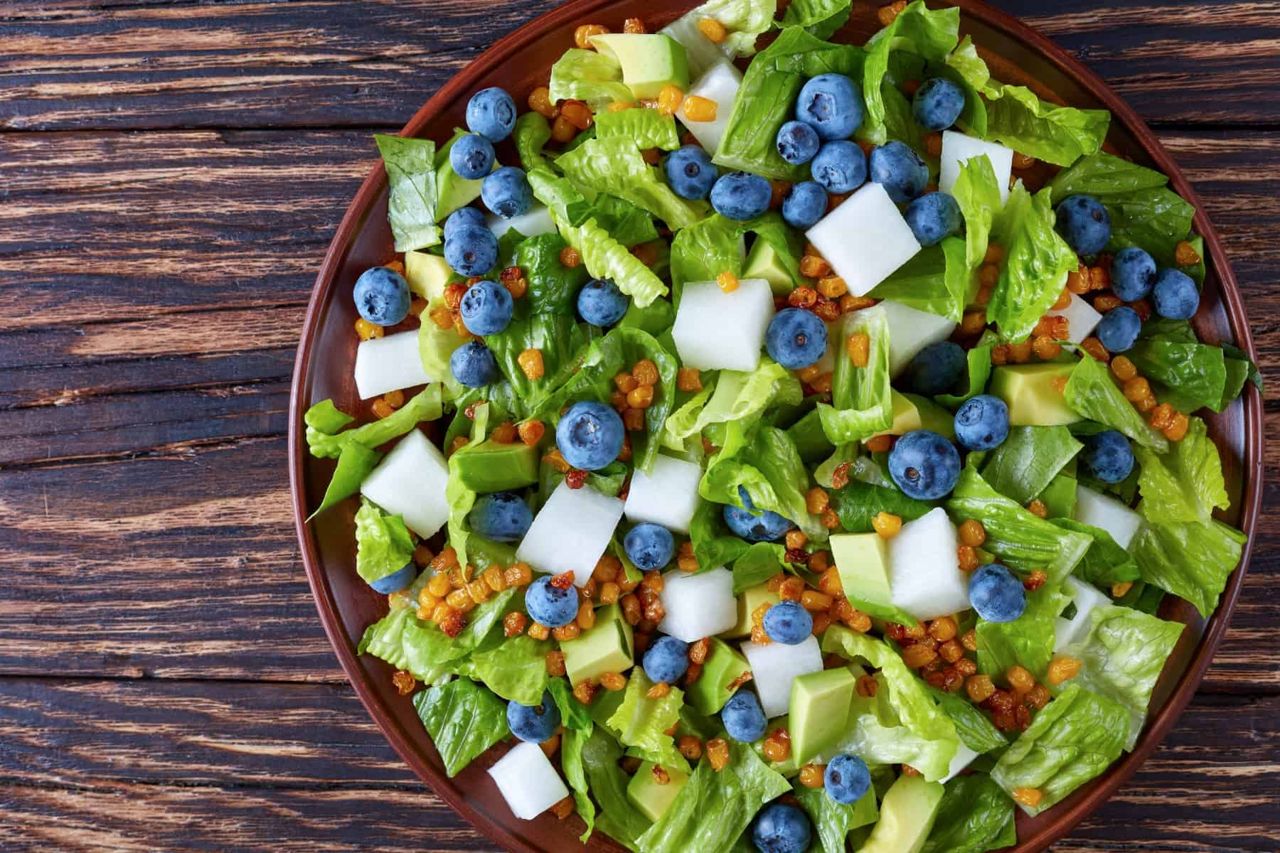 Mexican Salad with Blueberries, romaine lettuce leaves, jicama, roasted Corn kernels and Avocado on a clay plate on an old rustic wooden table, view from above, close-up, flatlay