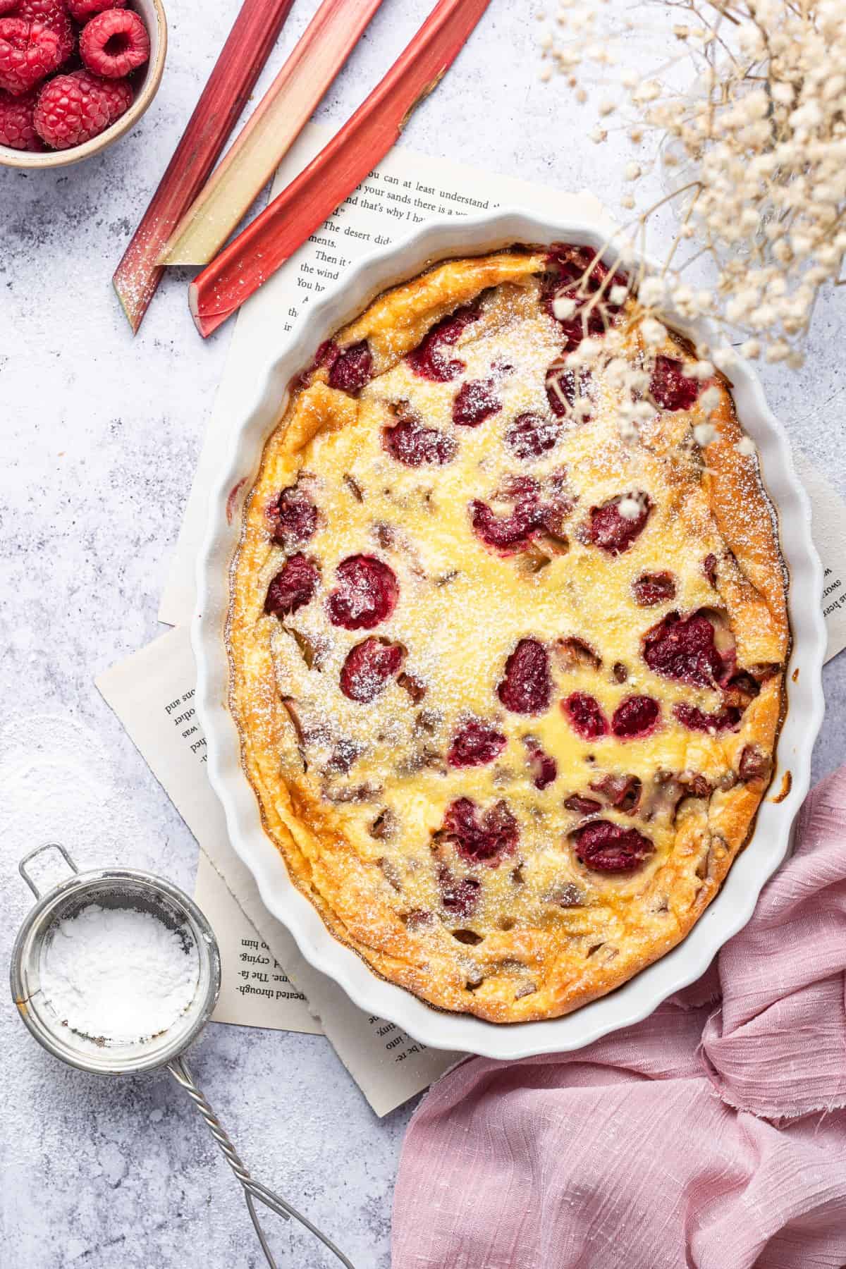 Clafoutis over recipe sheets, with rhubarb stalks and white flowers