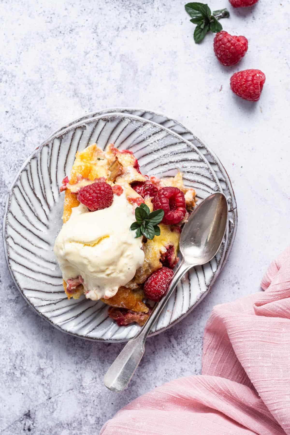 Rhubarb Raspberry clafoutis on a plate with ice cream, fresh raspberries and a mint sprig. 