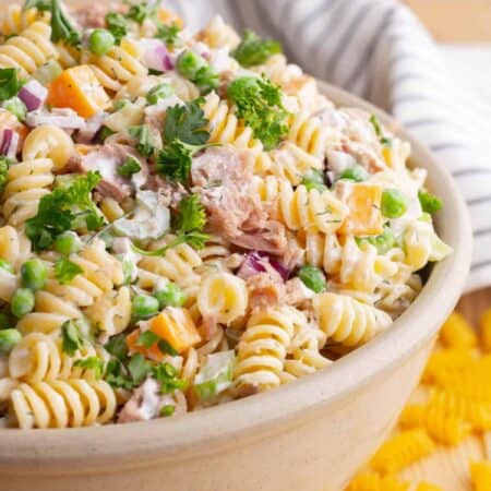 A serving bowl filled with rotini pasta, peas, tuna chunks, red onions, orange cheddar, and celery.