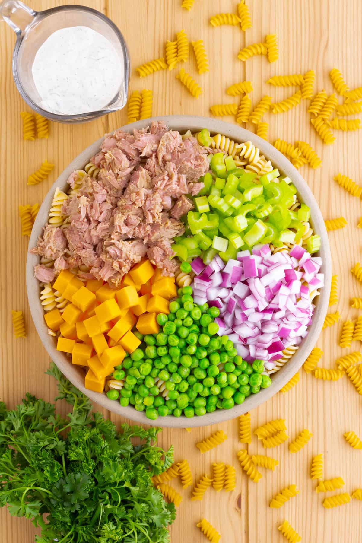 A bowl with tuna pasta salad ingredients divided into sections.
