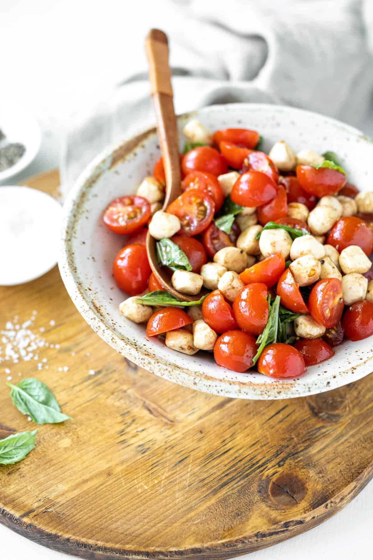 Bowl of caprese salad on a board with basil and salt