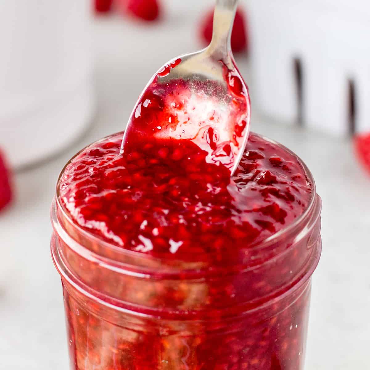 Pulling a spoon out of a jar of raspberry sauce