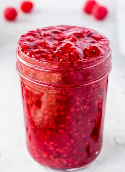 Jar of raspberry sauce that is overflowing.