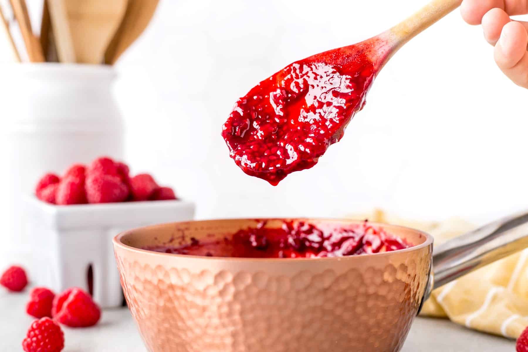 Horizontal bowl of a wooden spoon coming out of raspberry sauce. 
