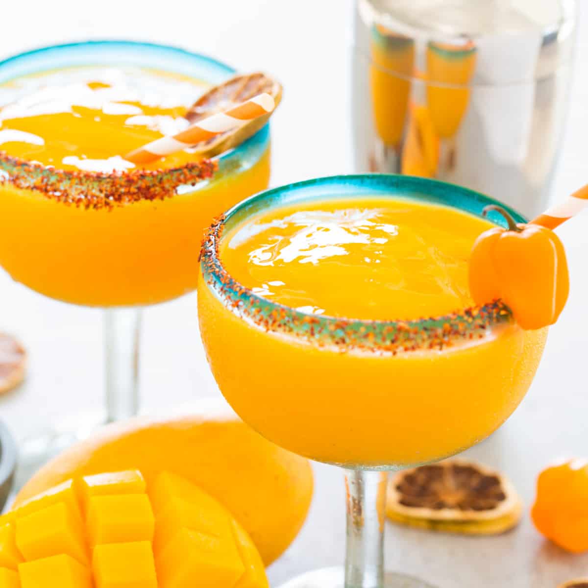 Two Mango Habanero Margaritas in glasses with garnishes and a fresh mango.
