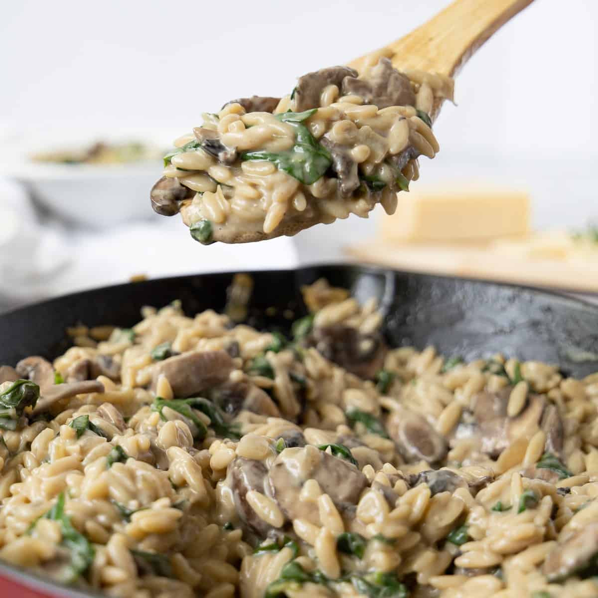 Close up of creamy mushroom orzo with spinach on wooden spoon over skillet.