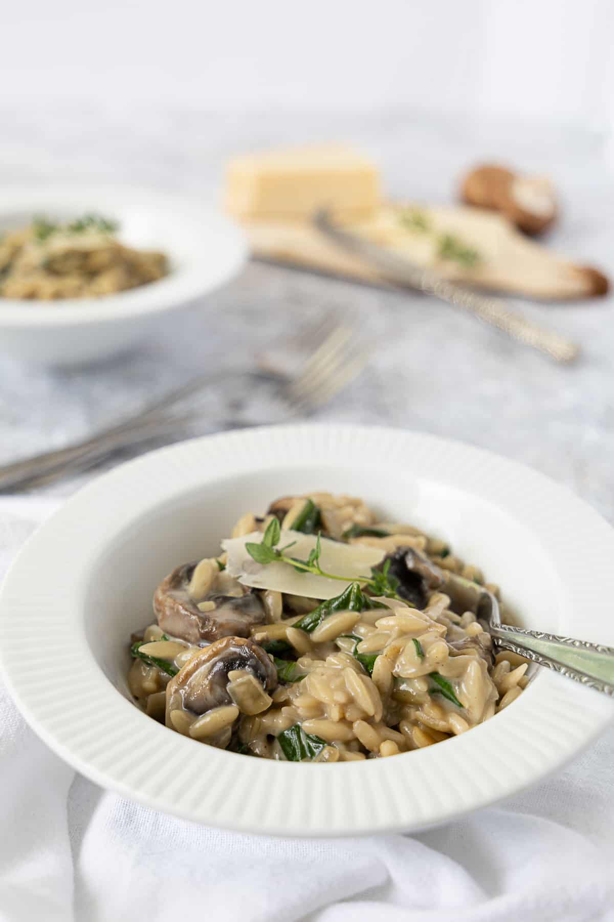 Side view of a serving of mushroom orzo with spinach topped with parmesan cheese