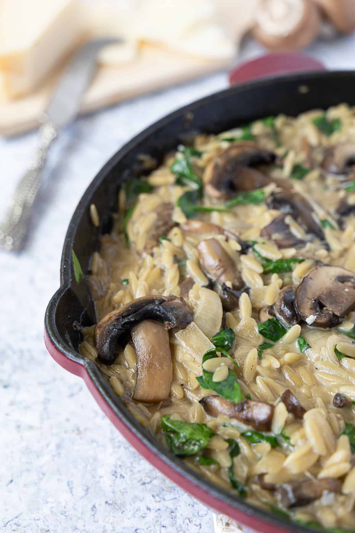 Close up of mushroom orzo in a skillet iron with the parmesan cheese in the back.