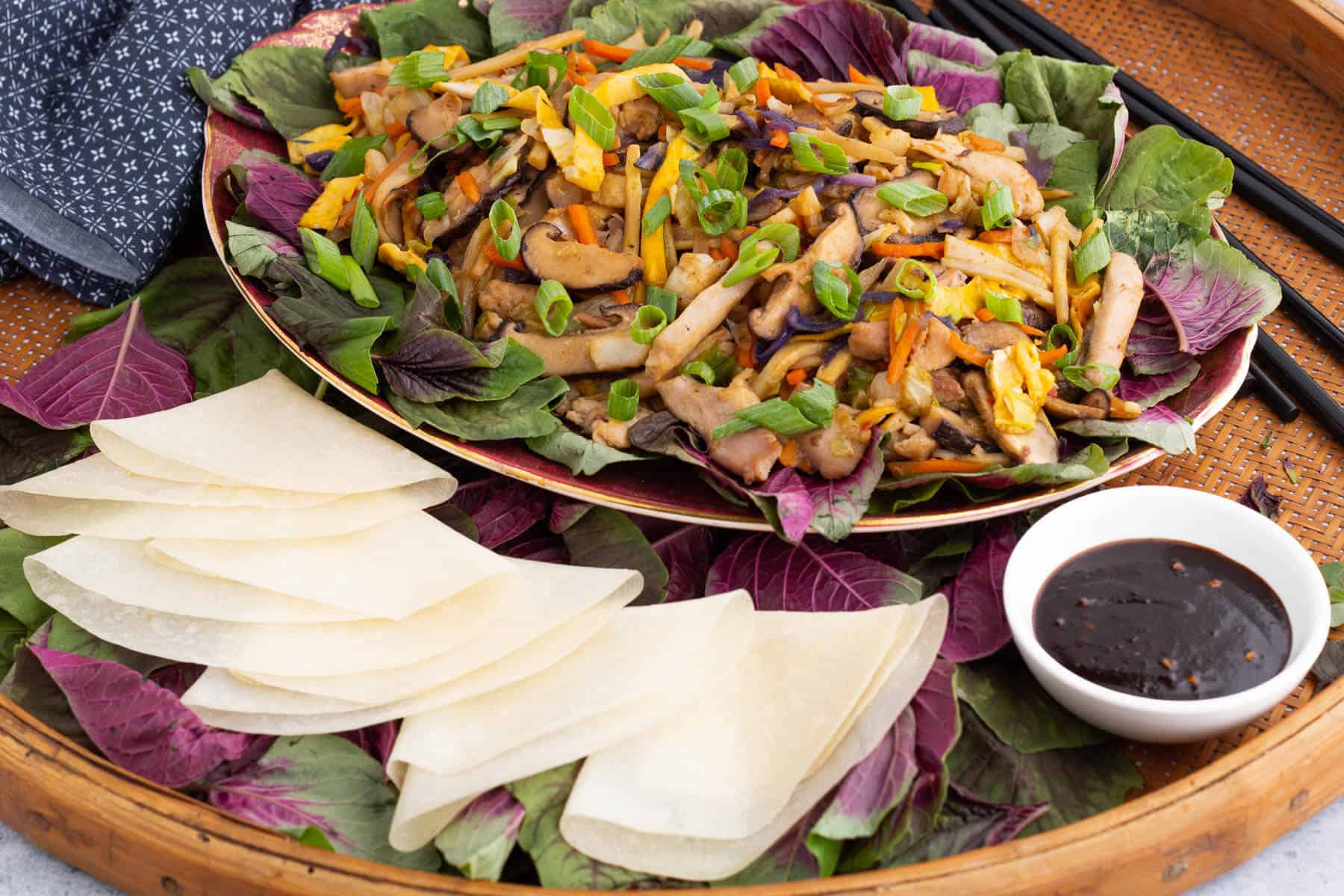 A platter full of colourful Moo Shu Chicken with Chinese pancakes and a dish of hoisin sauce.