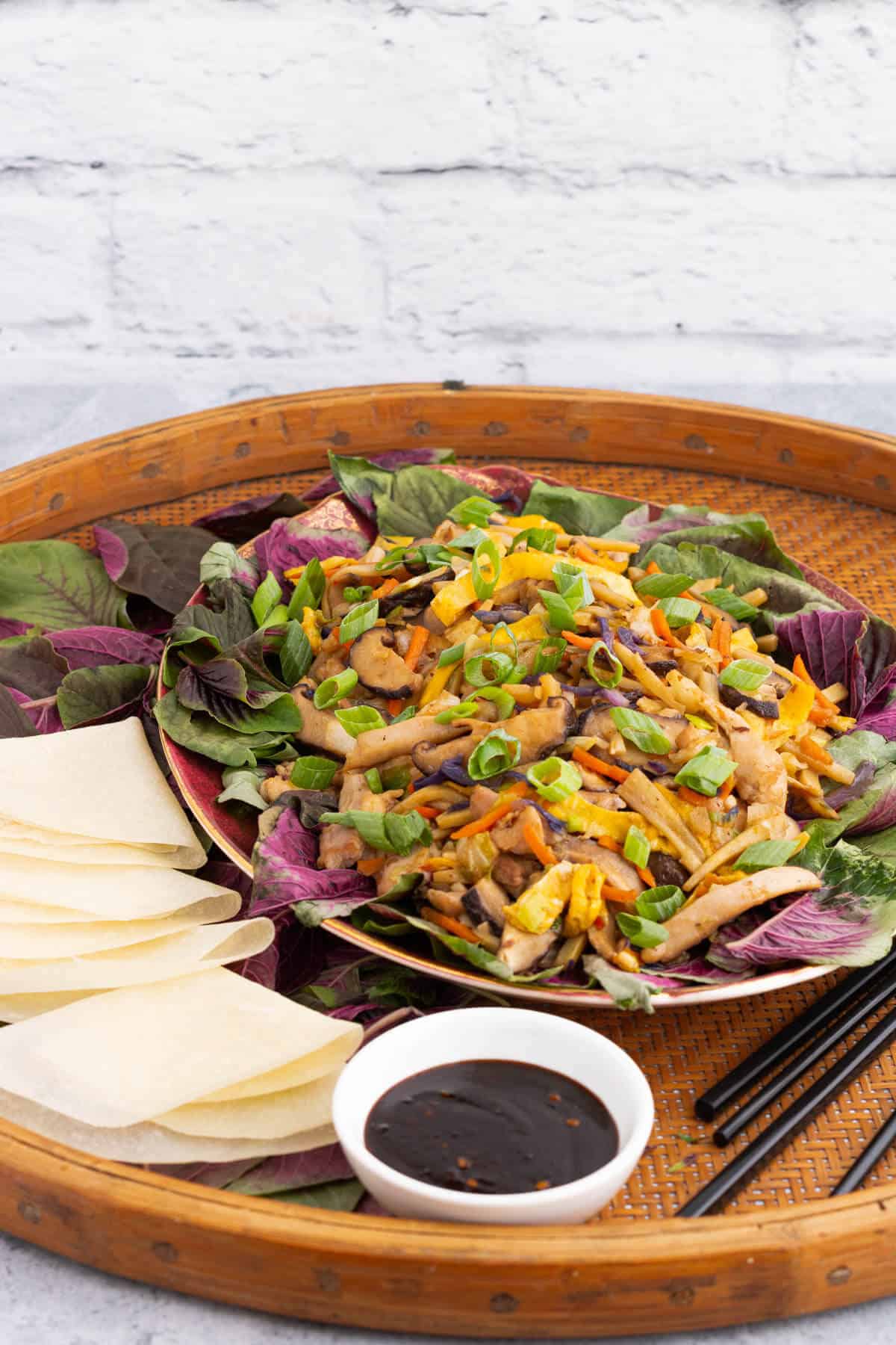 A platter full of colourful Moo Shu Chicken with Chinese pancakes and a dish of hoisin sauce.