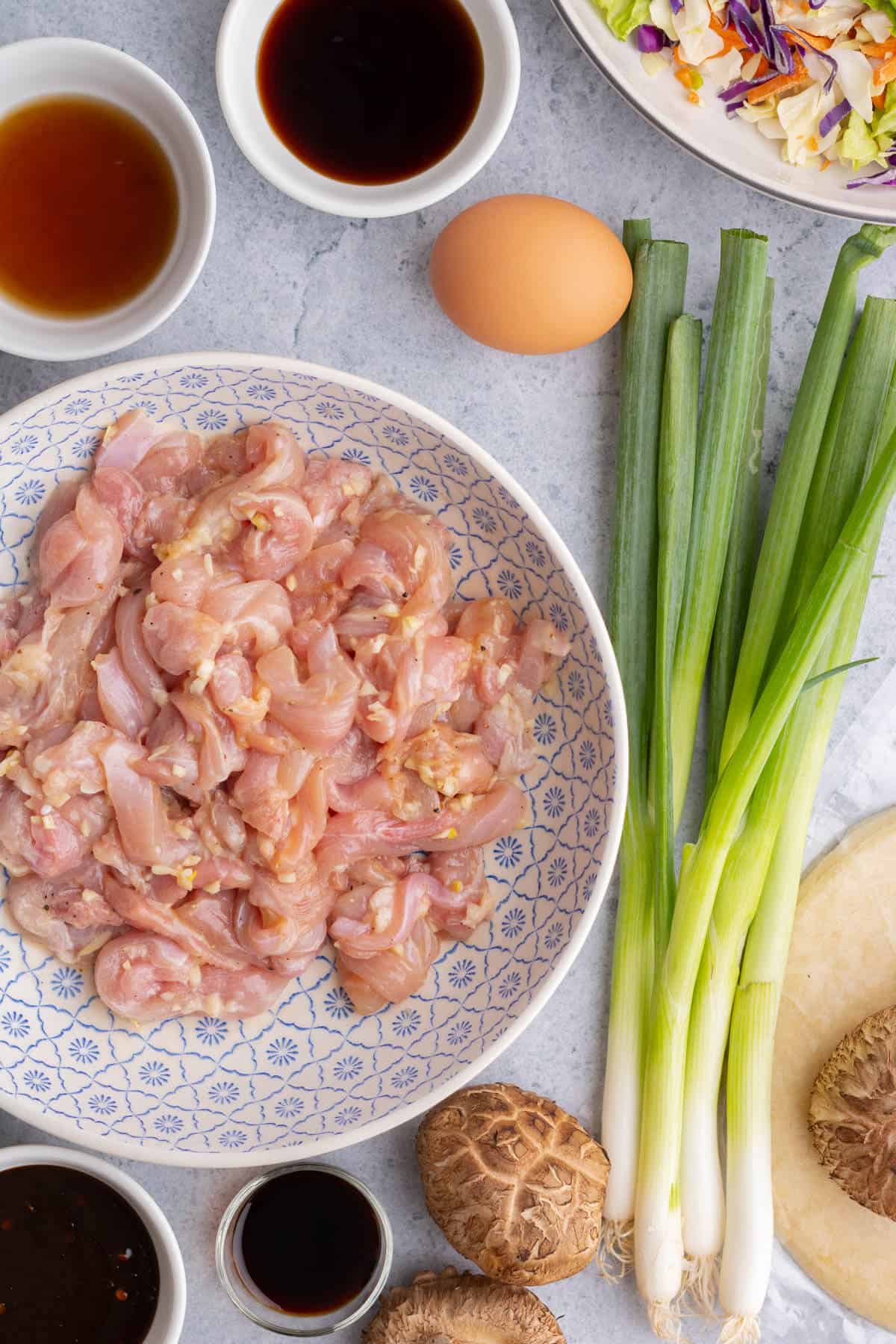 Sliced chicken marinating in a dish beside other Moo Shu ingredients.