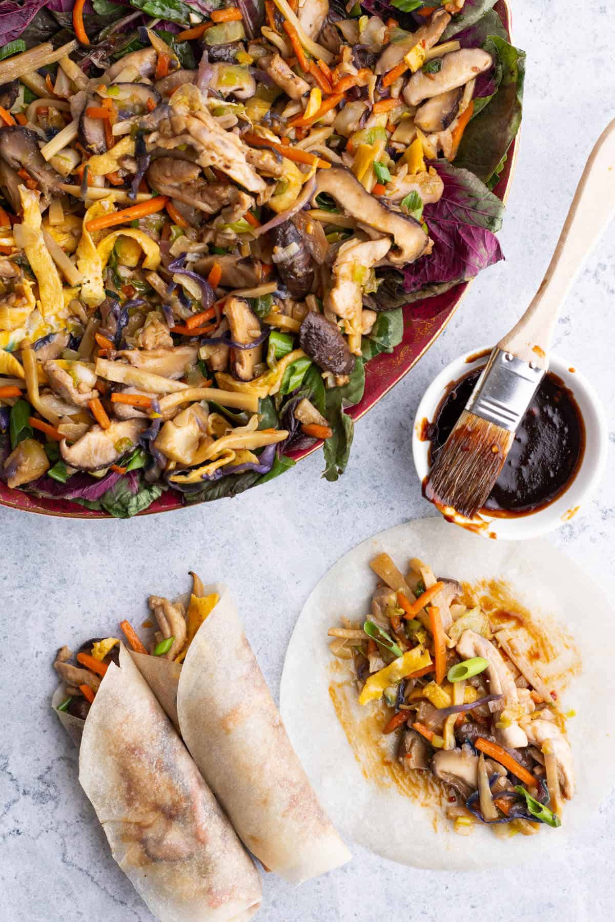 A platter full of colourful Moo Shu Chicken beside two rolled pancakes.