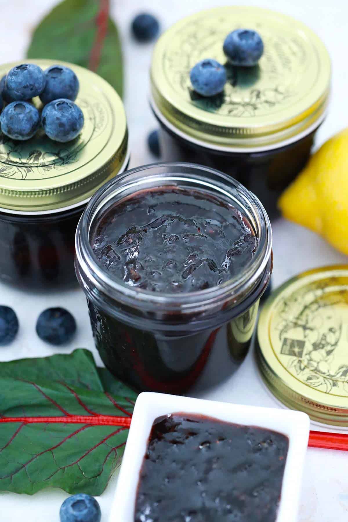 Jars of jam, one opened others with lids and blueberries on top