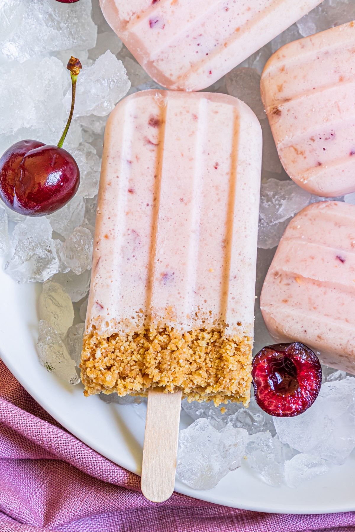 Overhead shot of Cherry Cheesecake Popsicles on ice with fresh cherries