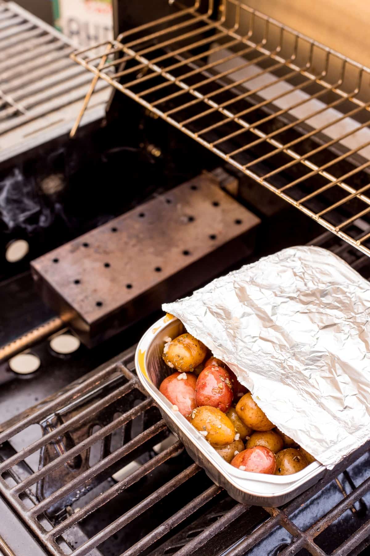Potatoes in a pan partially covered in foil on the grill. 