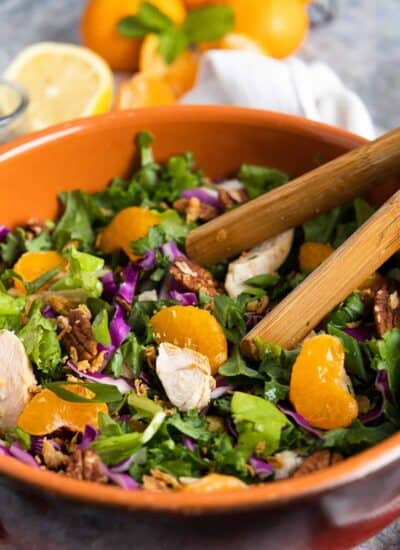 Mandarin chicken salad in a wooden bowl with tongs.