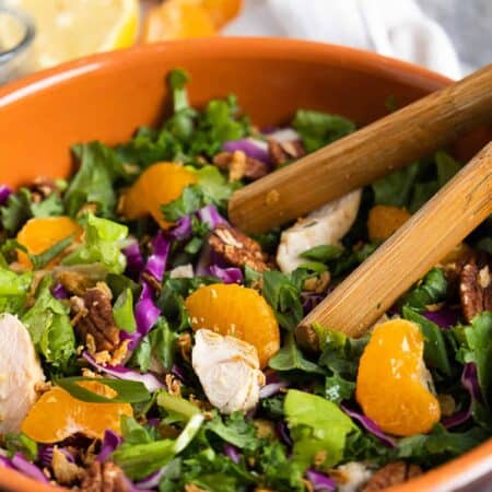 Mandarin chicken salad in a wooden bowl with tongs.
