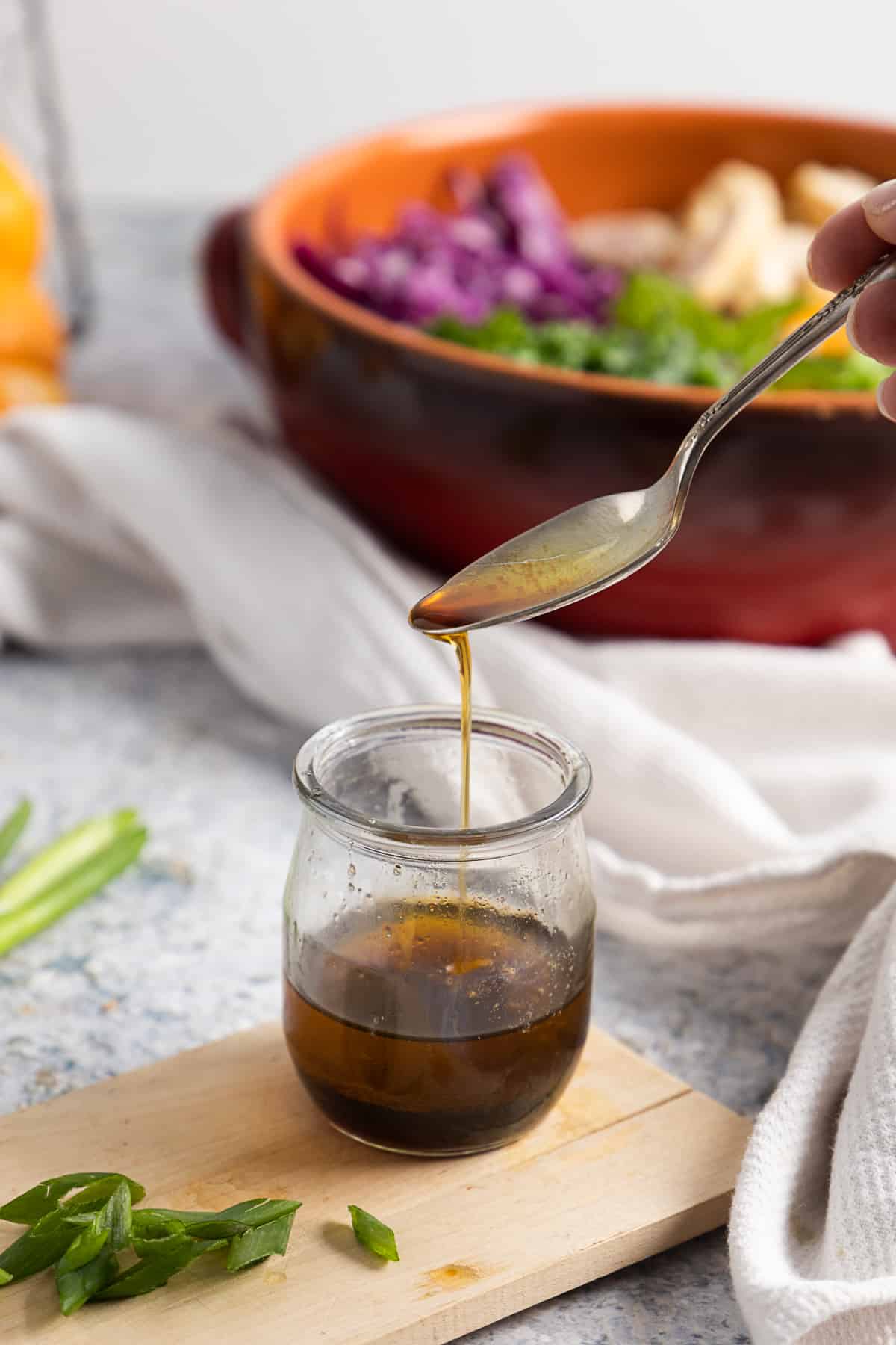 Side view of the Asian-inspired dressing in a glass jar with a drip from the spoon