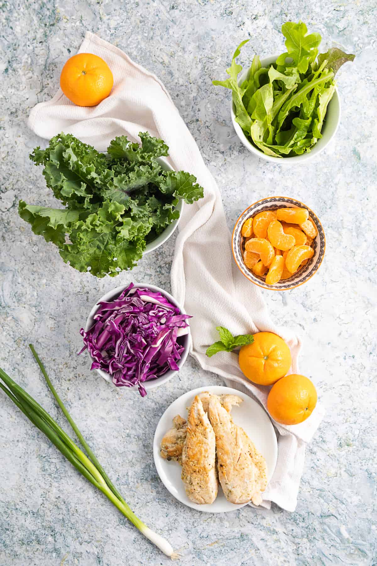 Top view of the ingredients for the mandarin chicken salad: kale, lettuce, mandarin, red cabbage, chicken