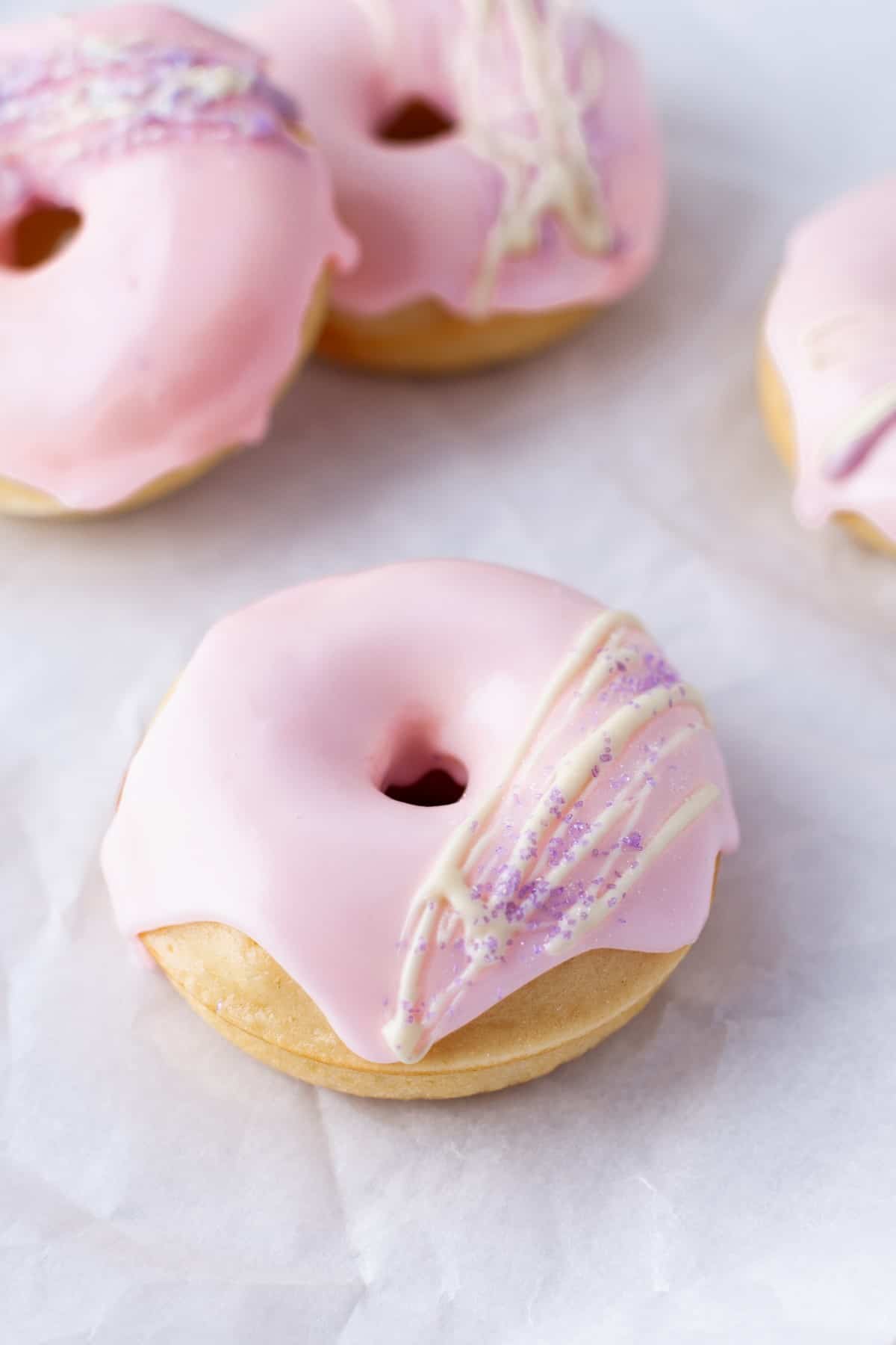 Picture of a Vanilla Baked Buttermilk Donut with pink icing, stripes and sprinkles. 