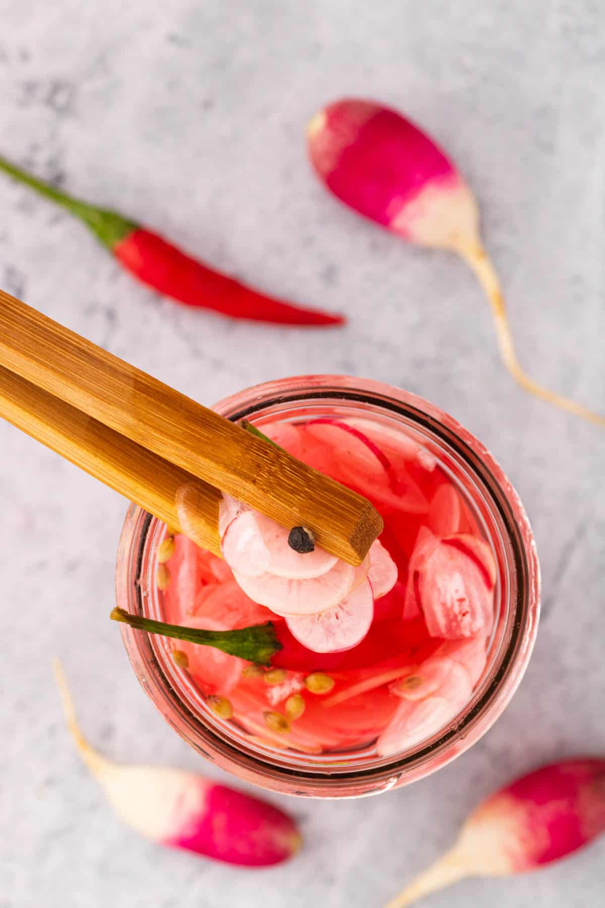 A pair of wooden tongs grabbing quick pickled radishes out of a jar.