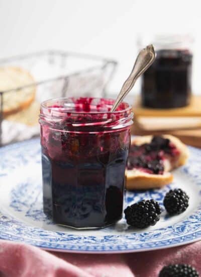 Side view of the jam jar with a spoon in it, placed on the blue plate and few fresh berries on the side.