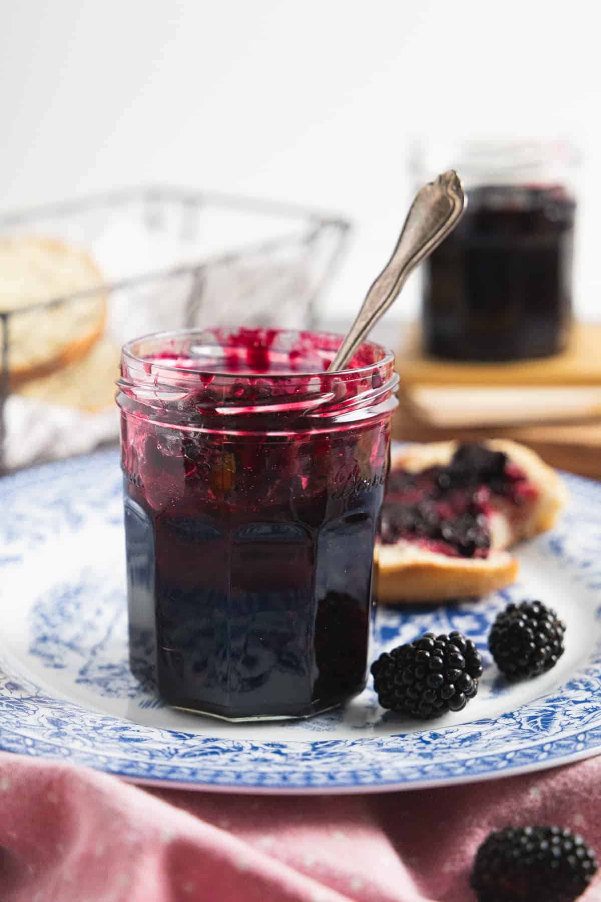 Side view of the jam jar with a spoon in it, placed on the blue plate and few fresh berries on the side. 