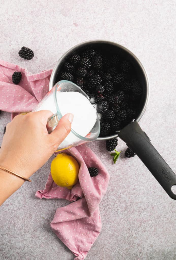 Adding sugar to blackberries in a pot