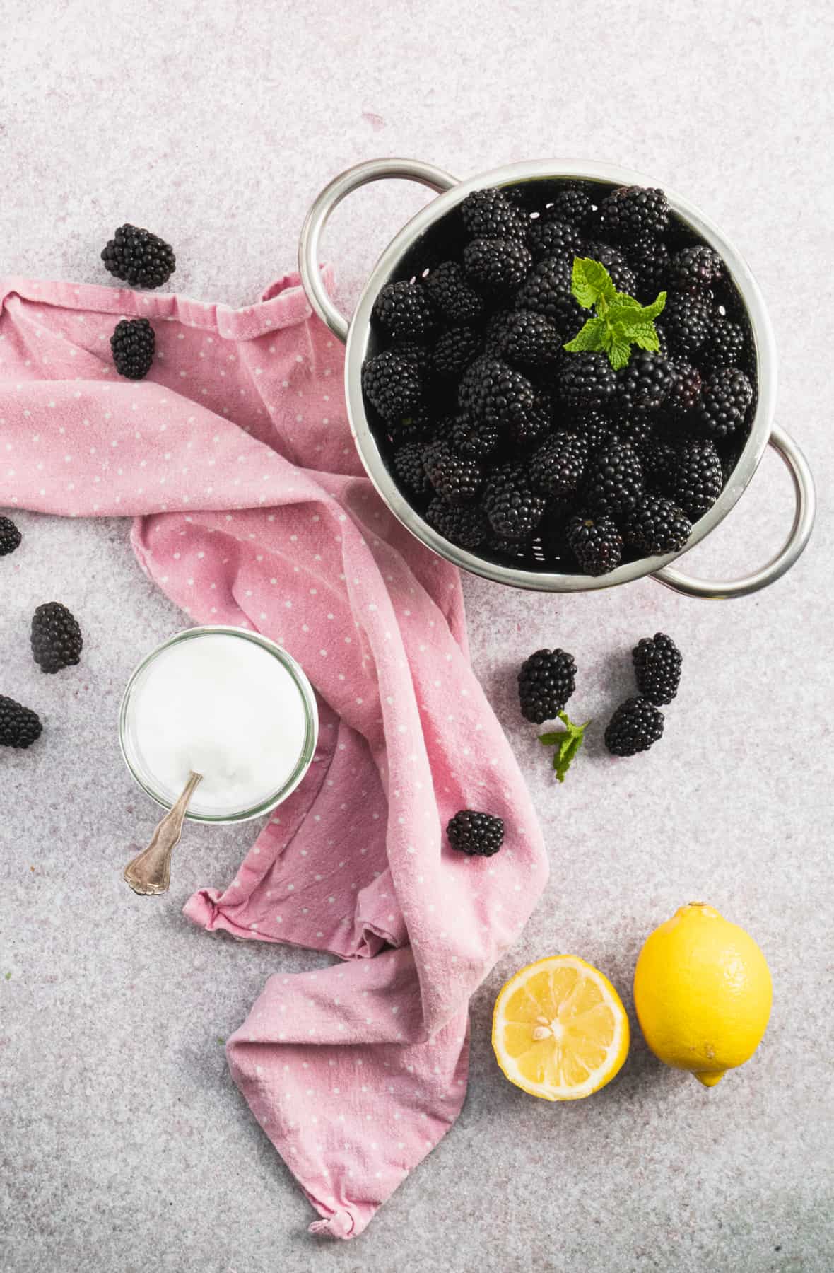 Top view of the ingredients to make jam, fresh blackberries in a colander, sugar and lemon.