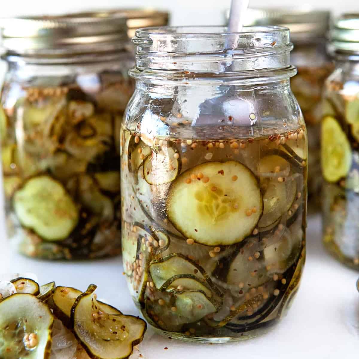 First jar is open with a fork and the rest are closed and filled with pickles
