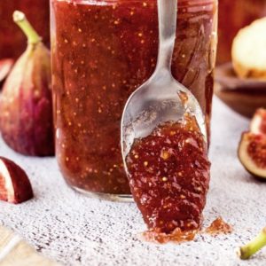 Fig jam on a spoon resting up against a jar of fig jam