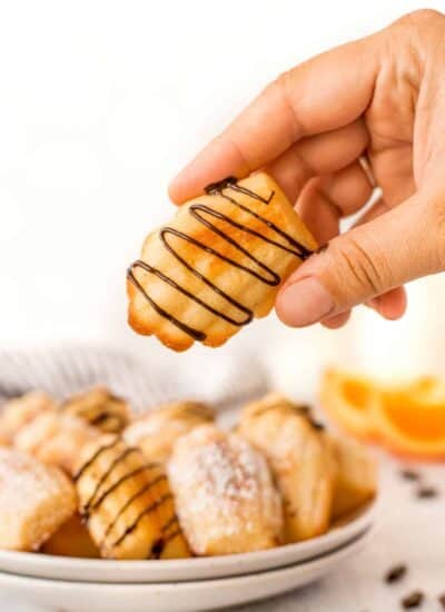 Holding an orange madeleine cookie with chocolate drizzle on it.