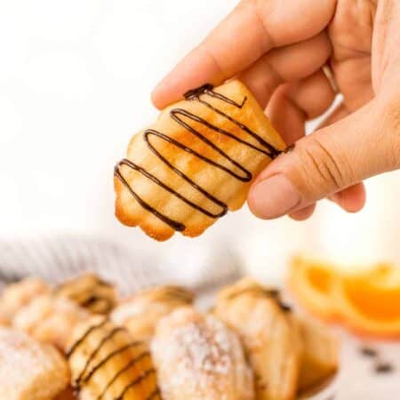 Holding an orange madeleine cookie with chocolate drizzle on it.