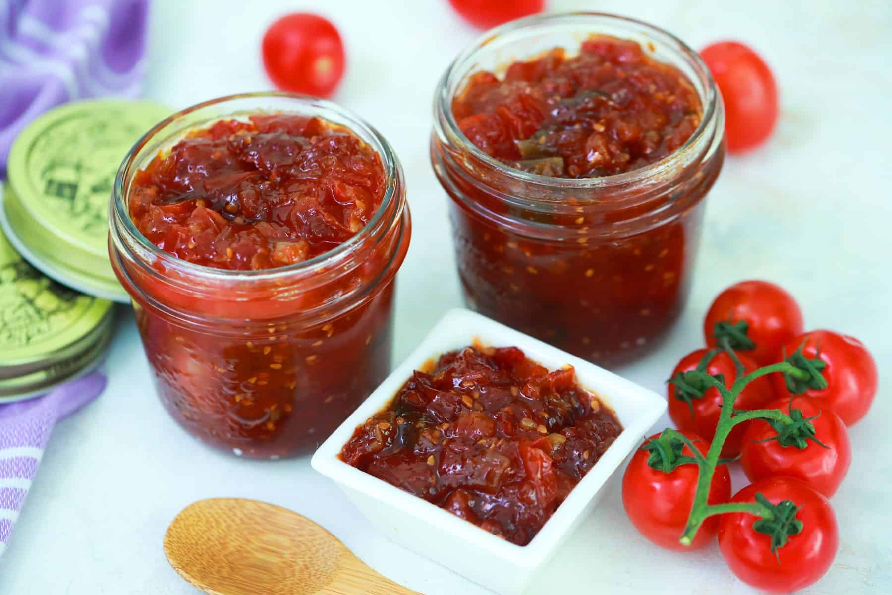 Tomato jam in jars and a white dish with small cherry tomatoes. 