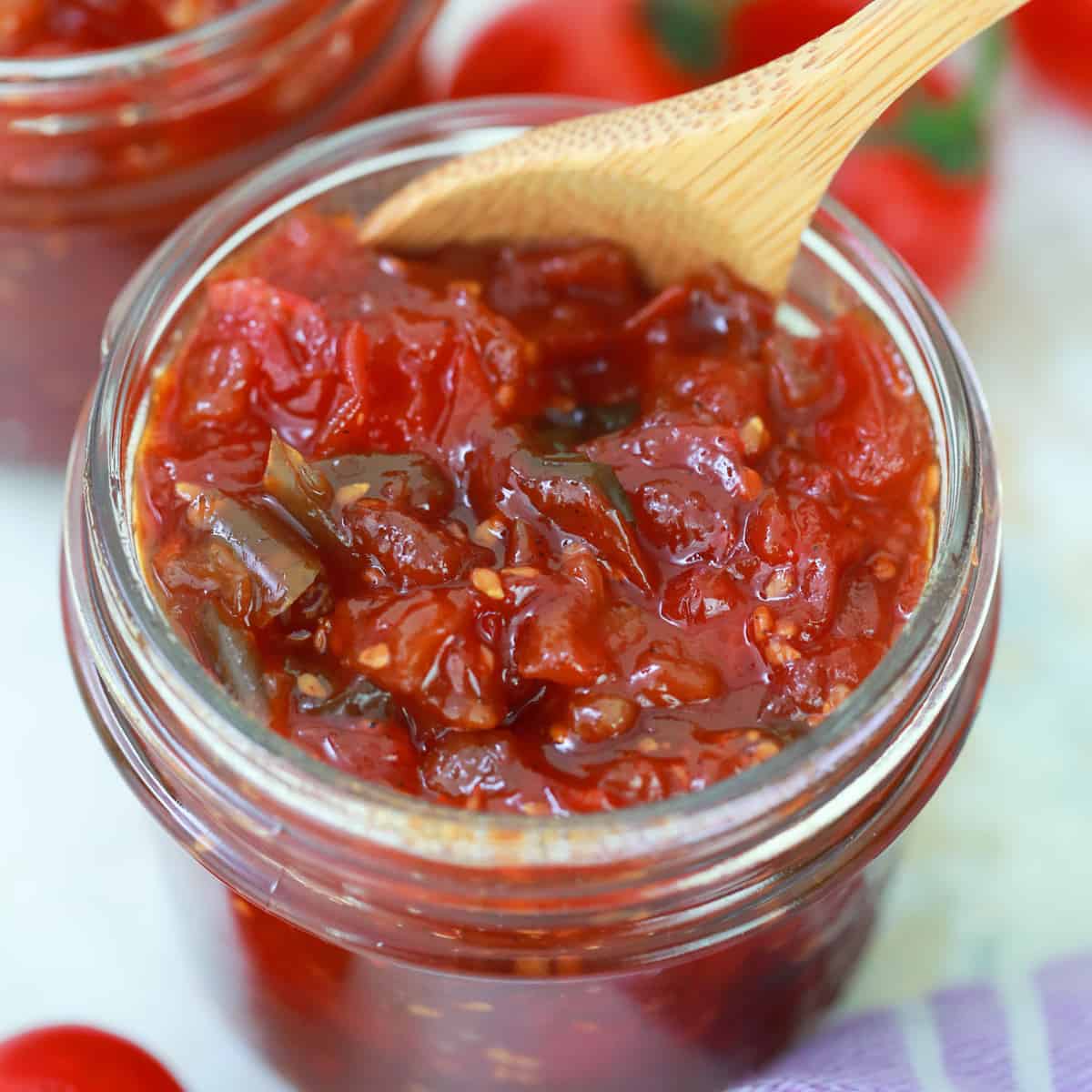 Overhead shot of tomato jam in a jar with a wooden spoon. 