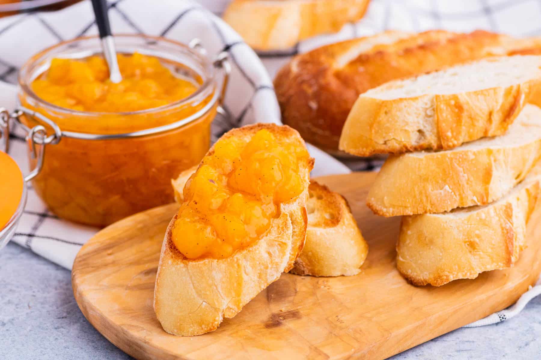 A toast covered in bright orange Peach Freezer Jam in front of a jar of the same jam.